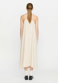 Leinen-Maxikleid in Off-White, mit dünnen Trägern und einer lockeren A-Linie, kombiniert mit schwarzen Schuhen und weißen Socken.