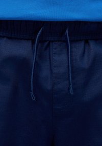 Merensinisen urheilushortsit, joissa on joustava vyötärönauha, säädettävä kiristysnauha ja sileä, kevyt kangaspinta.