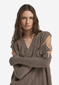 Brązowy sweter dziany z wzorem diamentowym, głębokim dekoltem w serek oraz prążkowanymi rękawami. Miękka faktura, dopasowany fason i logo na rękawie.