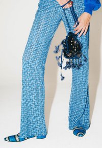 Pantaloni svasati con motivo geometrico blu, abbinati a una borsa nera in velluto decorata con ornamenti e nappine.