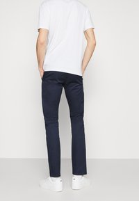 Pantalon bleu marine en mélange de coton, ajusté, avec une texture lisse. Porté avec un t-shirt blanc uni et des baskets blanches.