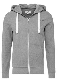 Sudadera gris con cremallera, fabricada en tejido suave, con un bolsillo frontal, cordones blancos y un sutil logotipo en la parte superior izquierda.