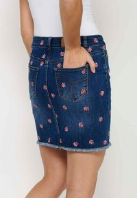 Denim krilo z rožnatim vezenjem v roza barvi, z oprijetim krojem, raztrganim robom in dvema zadnjima žepoma. Narejeno iz temno modrega blaga.