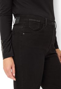 Jeans in denim nero con una vestibilità slim, caratterizzati da una vita testurizzata, chiusura con bottone metallico e dettagli di cucitura discreti sui taschini laterali.