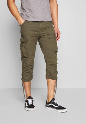 Pantalons cargo vert olive avec plusieurs poches, longueur raccourcie, poignets ajustables et texture lisse, associés à des baskets noires.