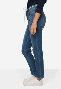 Siniset farkut suoran leikkauksen kanssa, jossa on valkoinen naru, hieman kulumista ja kaksi sivutaskua. Yhdistettynä valkoisiin tenniskenkiin.