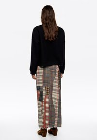 Jersey negro de gran tamaño con mangas largas, usado sobre una falda maxi de patchwork que presenta varios patrones de cuadros en tonos tierra. Botas marrones.