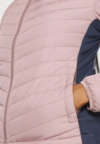 Różowa pikowana kurtka z granatowym bocznym panelem, wyposażona w frontowy zamek błyskawiczny, boczne kieszenie oraz elastyczne mankiety, wykonana z lekkiego materiału.