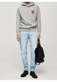 Grijze hoodie met een vooraanstaande graphic, lichtblauwe jeans en zwarte enkellaarsjes. Houdt een zwarte tas vast. Soepele textuur, eenvoudig ontwerp.