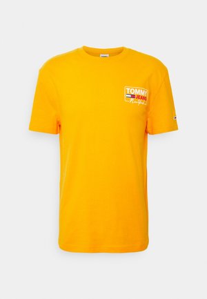 Maglietta a maniche corte di un giallo brillante con il logo "Tommy Jeans New York" sul petto e un piccolo emblema a forma di bandiera sulla manica sinistra.