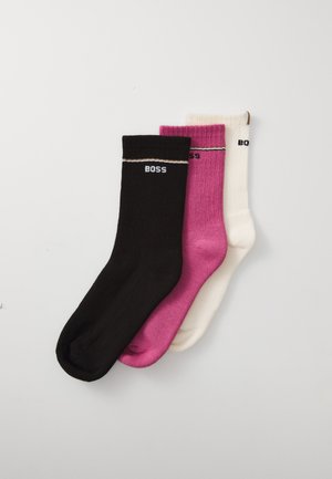 Trois paires de chaussettes côtelées en noir, rose et blanc, avec des rayures horizontales contrastantes et le logo "BOSS" imprimé sur chacune.