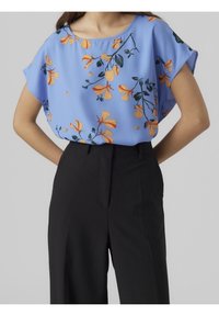 Sininen kukkaneule, jossa on lyhyet hihat ja keltaisia sekä oransseja kukkia, yhdistettynä mustiin korkeavyötäröisiin housuihin. Liukas kangas ja rento malli.