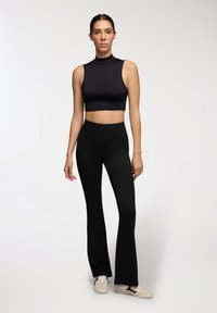 Czarny krótki bezrękawnik i czarne spodnie z wysokim stanem w fasonie dzwonów wykonane z elastycznego materiału, noszone z jasnymi trampkami.