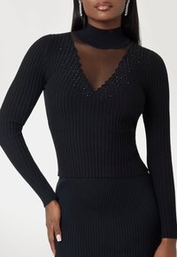 Black ribbed long-sleeve top with a sheer V-neckline and scalloped edge, featuring subtle shimmer and a fitted silhouette.