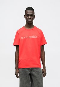 Czerwony bawełniany t-shirt z krótkimi rękawami i okrągłym dekoltem, z nazwą marki „marimekko” nadrukowaną jasnobeżowym kolorem na przodzie.