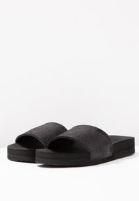 Black slide sandals with textured upper and smooth sole. Wide straps for comfort, featuring a flat, low-profile design. Suitable for casual wear.