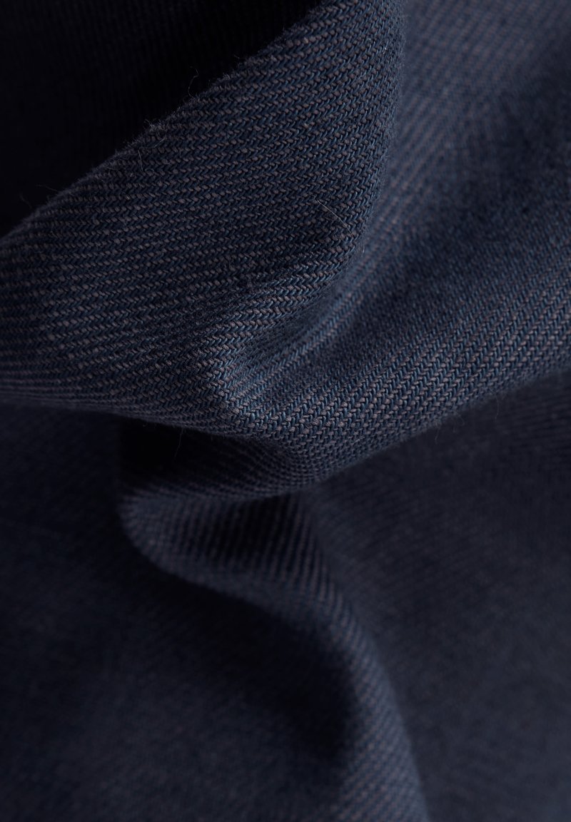 Donker marineblauwe stof met een gladde textuur, voorzien van geweven patronen en zachte, geplooide randen. Het materiaal lijkt duurzaam en buigzaam.