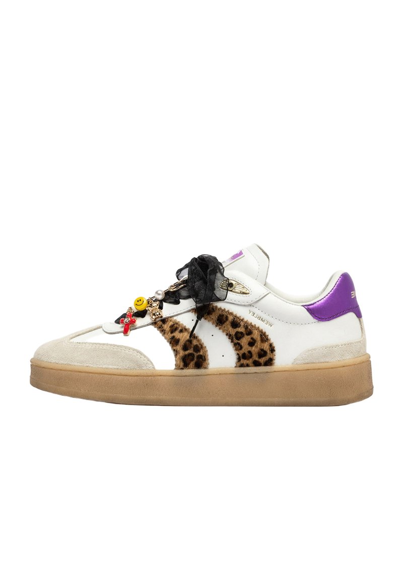 Sneaker bianco con strisce leopardate, linguetta viola, suola beige, lacci neri a nastro e dettagli decorativi tra cui una faccina sorridente e una croce.