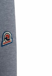 Grå tekstil med en blød tekstur har et cirkulært broderet patch i rød, blå og hvid, der viser et logo i nederste venstre hjørne.