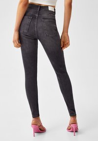 Jeans negros de cintura alta y ajustados, con una textura suave, dos bolsillos traseros y tacones rosas con tiras. Enfócate en la silueta elegante.