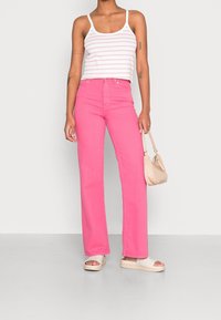 Różowe dżinsy w szerokim kroju z wysokim stanem, zestawione z białą i różową tank topami w paski. Uzupełnione małą beżową torebką i sandałami.