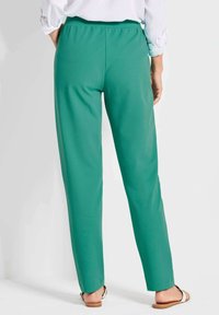 Groene, loszittende broek met een elastische tailleband, met een zachte textuur en een rechte pijpdesign, gecombineerd met platte sandalen.