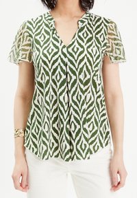 Grøn- og hvidmønstret bluse med korte, gennemsigtige ærmer og V-hals. Har et geometrisk design og en afslappet pasform.