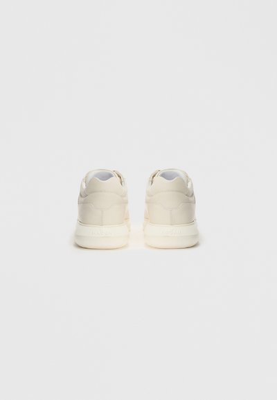 Beige sneakers with white soles shown from the back on a plain white background, displaying brand name embossed on the heel.