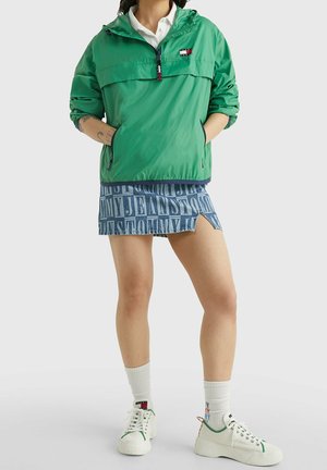 Zielona bluza z długim rękawem, z półzamkiem, kapturem i bocznymi kieszeniami. Połączona z niebieską mini spódnicą dżinsową z dużymi białymi napisami.