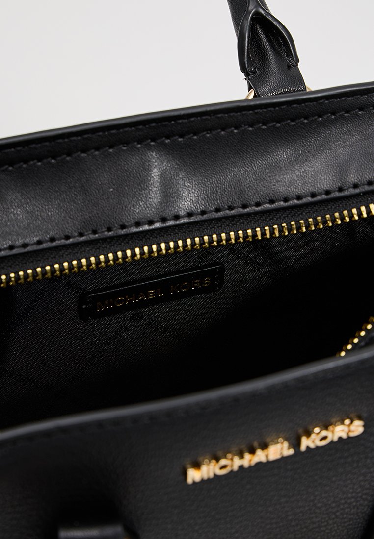Intérieur d'un sac à main en cuir noir avec une fermeture éclair dorée, doté d'une doublure en tissu et d'une étiquette avec le logo "MICHAEL KORS" sur le côté.