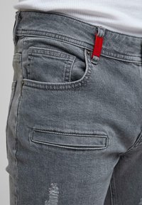 Harmaat farkut ovat slim fit -malliset, niissä on minimaalinen kuluminen, punainen etiketti vyötäröllä, perinteiset taskut ja yksi sääri on kulutettu.