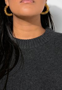 Pendientes de aro de oro con un diseño espiral texturizado, combinados con un suéter de punto acanalado gris oscuro que tiene un escote redondo.