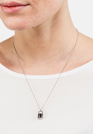 Silberne Halskette mit einem kleinen, glänzenden Vorhängeschloss-Anhänger. Die Kette ist dünn und zart, mit einer glatten Textur. Getragen über einem weißen Oberteil.