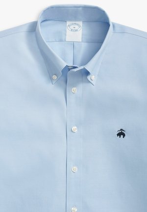 Camicia azzurra chiara con colletto, dotata di bottoni bianchi e un piccolo logo ricamato nero sul lato sinistro del petto.