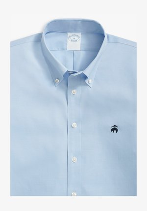 Camicia azzurra chiara con colletto, dotata di bottoni bianchi e un piccolo logo ricamato nero sul lato sinistro del petto.