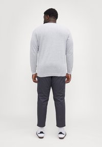 Grauer gestrickter Pullover mit langen Ärmeln, kombiniert mit dunkler Cargo-Hose; weiße Sneaker mit schwarzen Akzenten runden das Outfit ab.