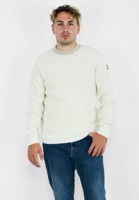 Maglione bianco a coste con maniche lunghe, scollatura rotonda e finitura testurizzata, abbinato a jeans in denim blu.