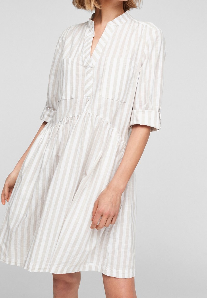 Robe légère à rayures avec une patte de boutonnage, un col, deux poches poitrine et des manches retroussées dans des tons doux de beige et de blanc.