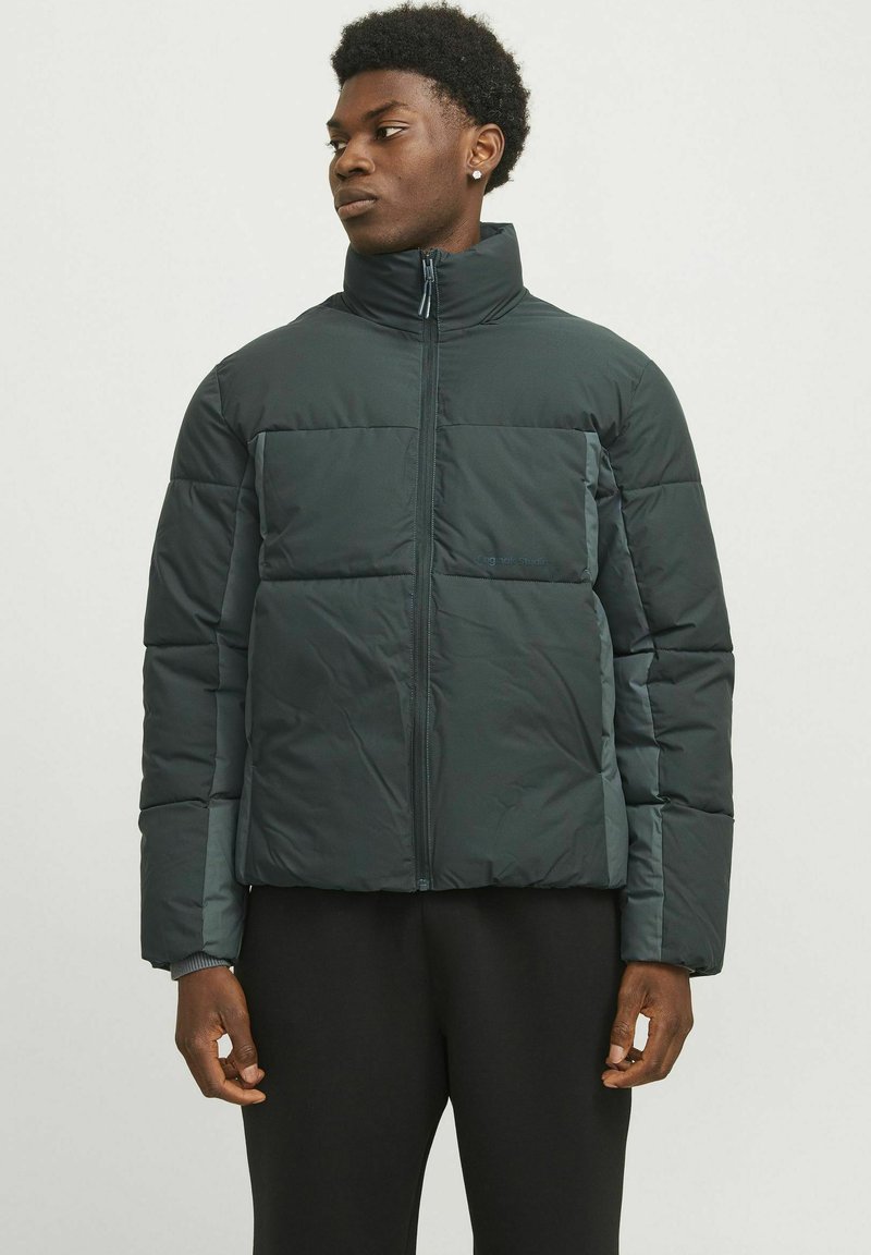 Dunkelgrüne gepolsterte Jacke mit hohem Kragen, Frontreißverschluss und kontrastierender Ärmelfaser. Verfügt über ein kastiges Design und dezente Markenkennzeichnung.