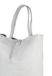 Witte leren totebag met dubbele handvatten en een dunne trekkoordsluiting aan de bovenkant tegen een witte achtergrond.