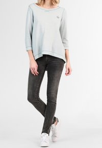 Světle modrý dlouhý rukáv top s kulatým výstřihem a jemnými švy, doplněný o tmavě šedé skinny džíny a bílé tenisky.