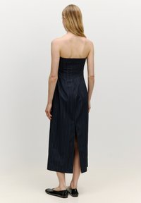 Ärmelloses, marineblaues Kleid mit Streifen, tailliertem Oberteil und einem Schlitz hinten; glatte Textur mit einer bescheidenen Länge und klaren Linien.