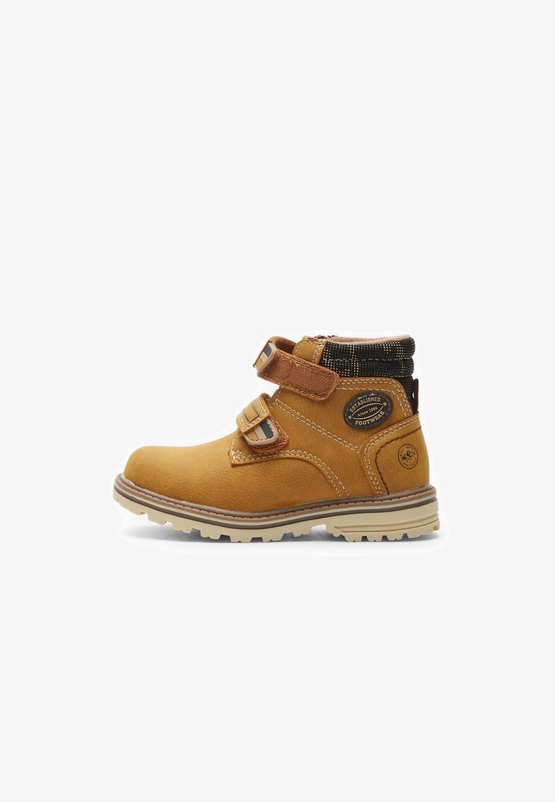 Bottine en cuir marron avec deux straps réglables, tissu noir texturé au niveau du col, et semelle en caoutchouc beige avec un motif de traction.
