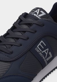 Αθλητικό παπούτσι Emporio Armani EA7 σε ναυτικό μπλε χρώμα με υφασμάτινη υφή, συνθετικά επικάλυψης, κλείσιμο με κορδόνια και λογότυπο της μάρκας στη γλώσσα και την πλευρική επιφάνεια.