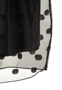 Svart genomskinlig tyg med större svarta prickar ovanpå ogenomskinligt svart tyg, som visar kontrasten mellan solida och transparenta material.