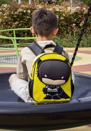 Mochila temática de Batman en color amarillo, con un diseño de personaje en 3D en la parte frontal, detalles en negro y cierres de cremallera. Textura suave, forma compacta.