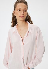 Lys pink skjorte med lange ærmer og en afslappet pasform. Blødt, struktureret stof med standard krave og subtilt vandret mønster.