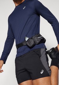 Merinavärinen långärmad skjorta, svarta shorts med grå detaljer och ett svart midjebälte som håller en vattenflaska. Athletic fit, lättviktsmaterial.