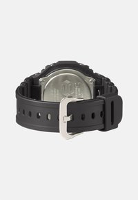 Bracelet de montre en silicone noir avec une boucle en métal argenté, design texturé moulé et trous de taille ajustables. L'arrière est en acier inoxydable.