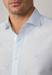 Camicia a righe blu chiaro con colletto button-down, realizzata in cotone. Presenta un piccolo accento blu ricamato sul petto.
